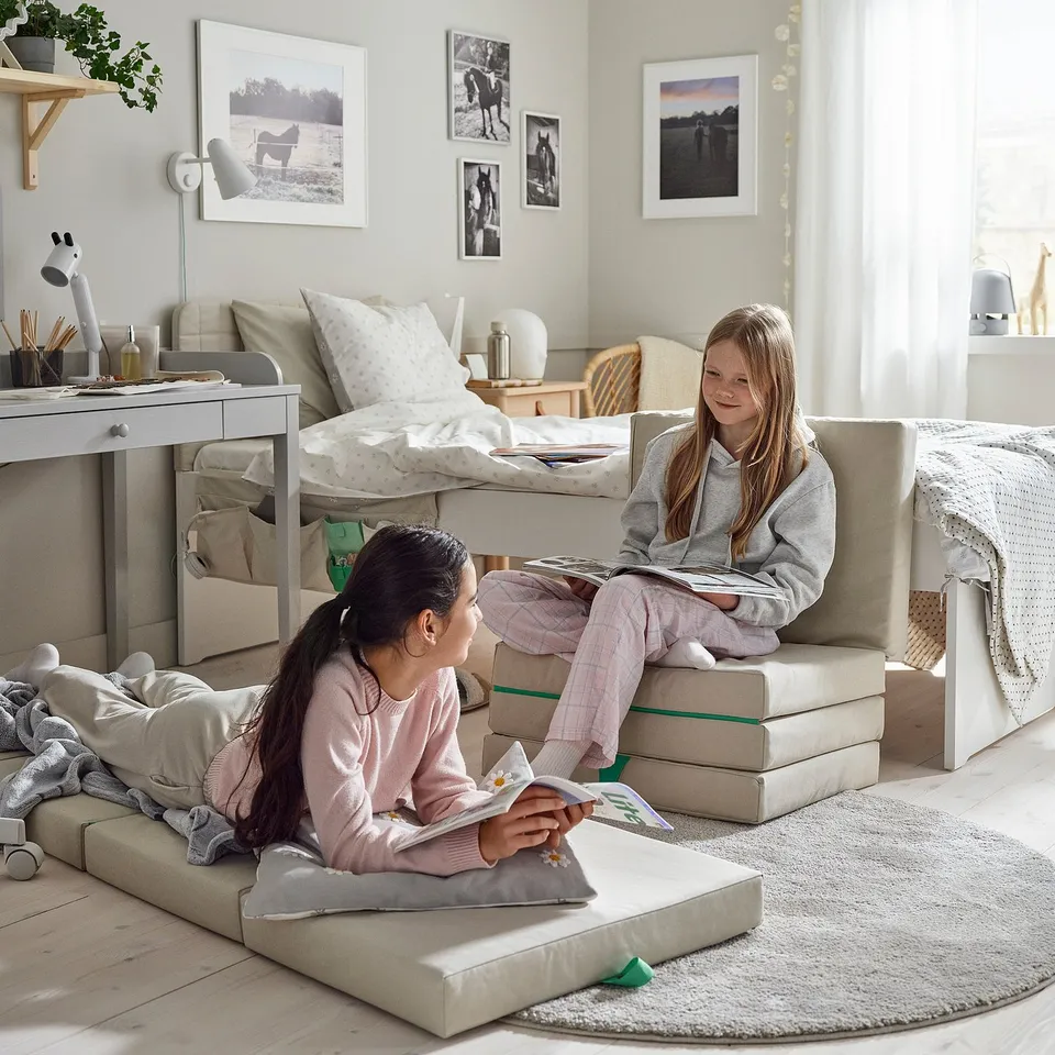 Girls sit on folding mattresses in a bedroom, reading books together.