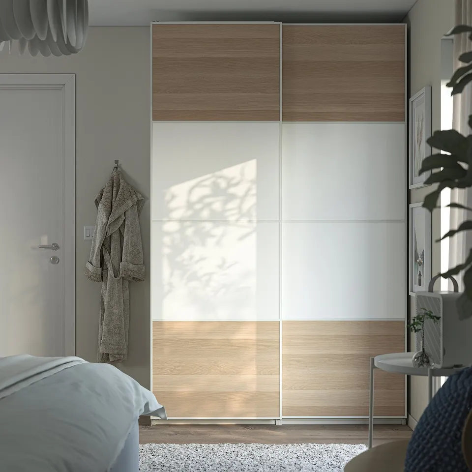Modern bedroom with large PAX wardrobe in natural wood and white. Sliding doors save space, grey bed linens, hanging robe, and potted plant nearby.