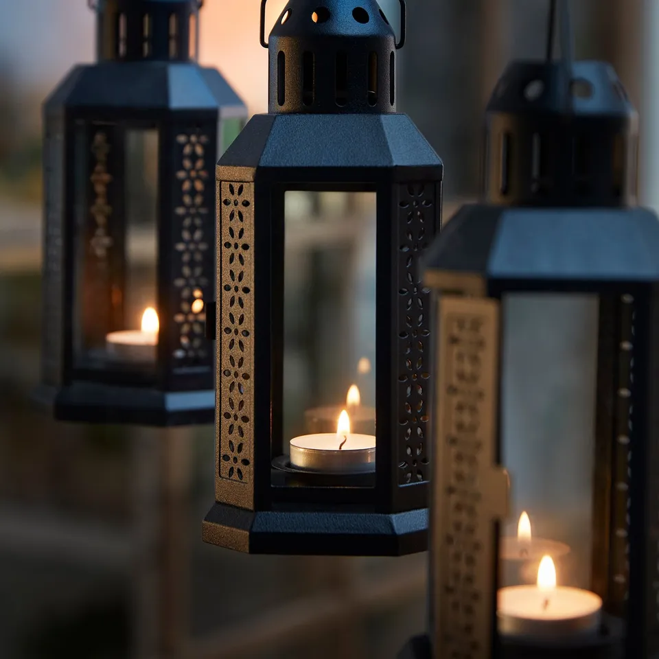 Black metal lanterns with intricate designs, holding tealights, emit soft, warm light.