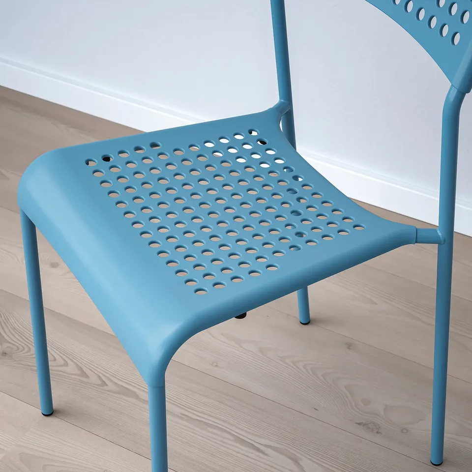 Blue plastic chair with circular holes in seat and back, placed on wooden floor, modern design, stackable.