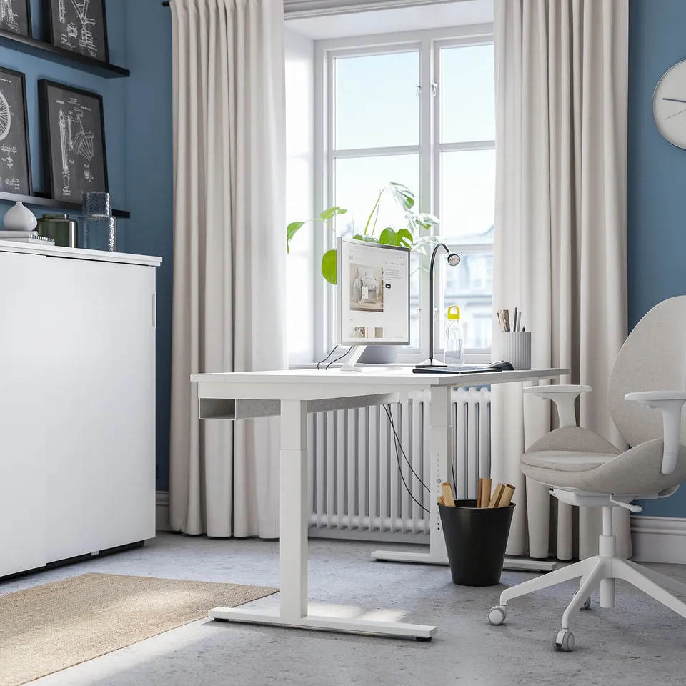 Modern home office with adjustable MITTZON desk, chair, & decor. Blue walls, large window, minimalist.