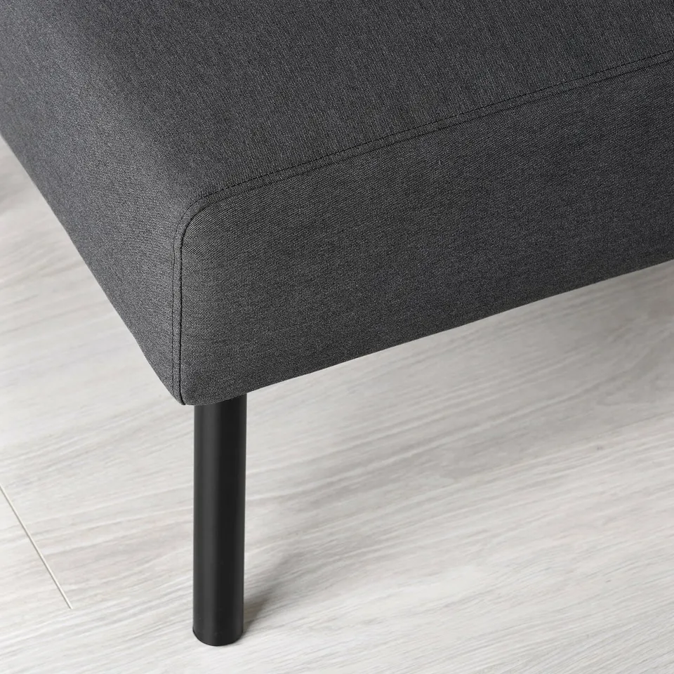 A modern footstool with sleek, black metal legs and a dark grey upholstered seat, placed on a light wooden floor.