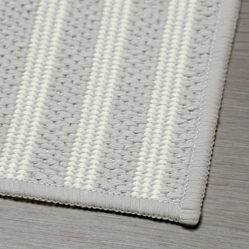 Grey chequered kitchen mat, well-crafted with stitched edges, laid on a striped surface.