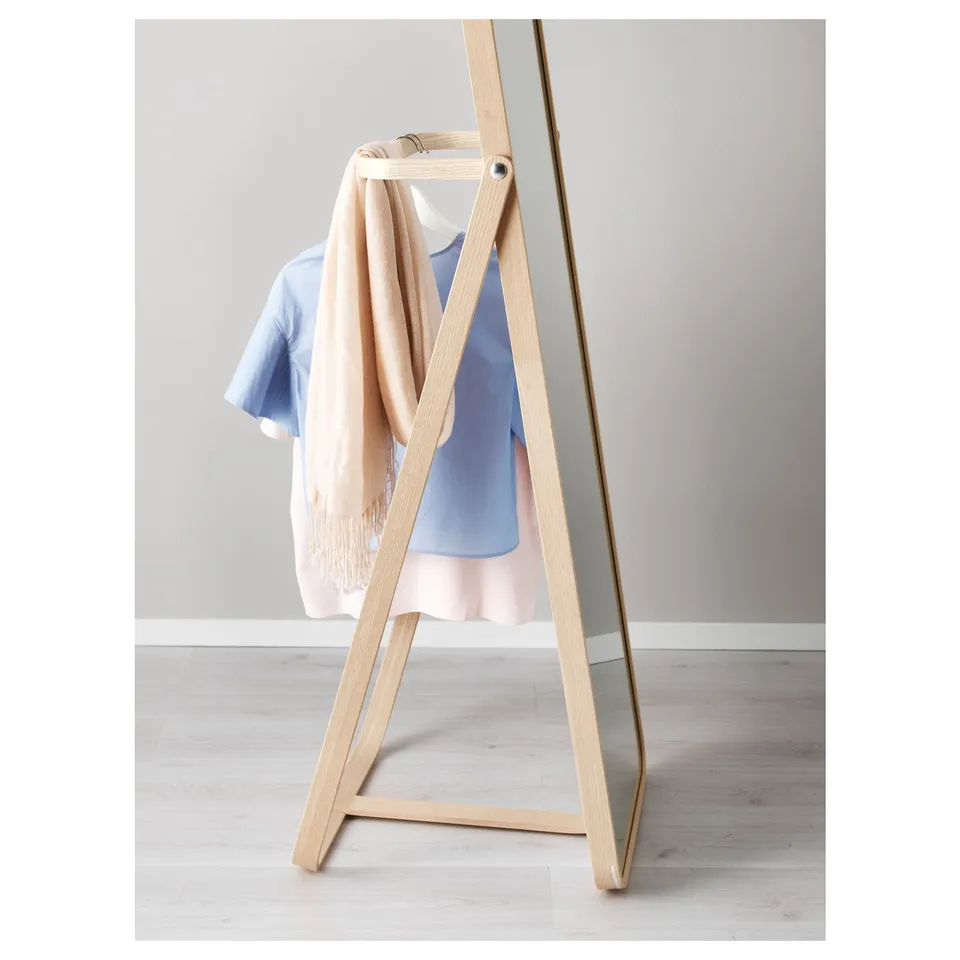 Floor mirror with clothes hook, displaying light outfit behind.