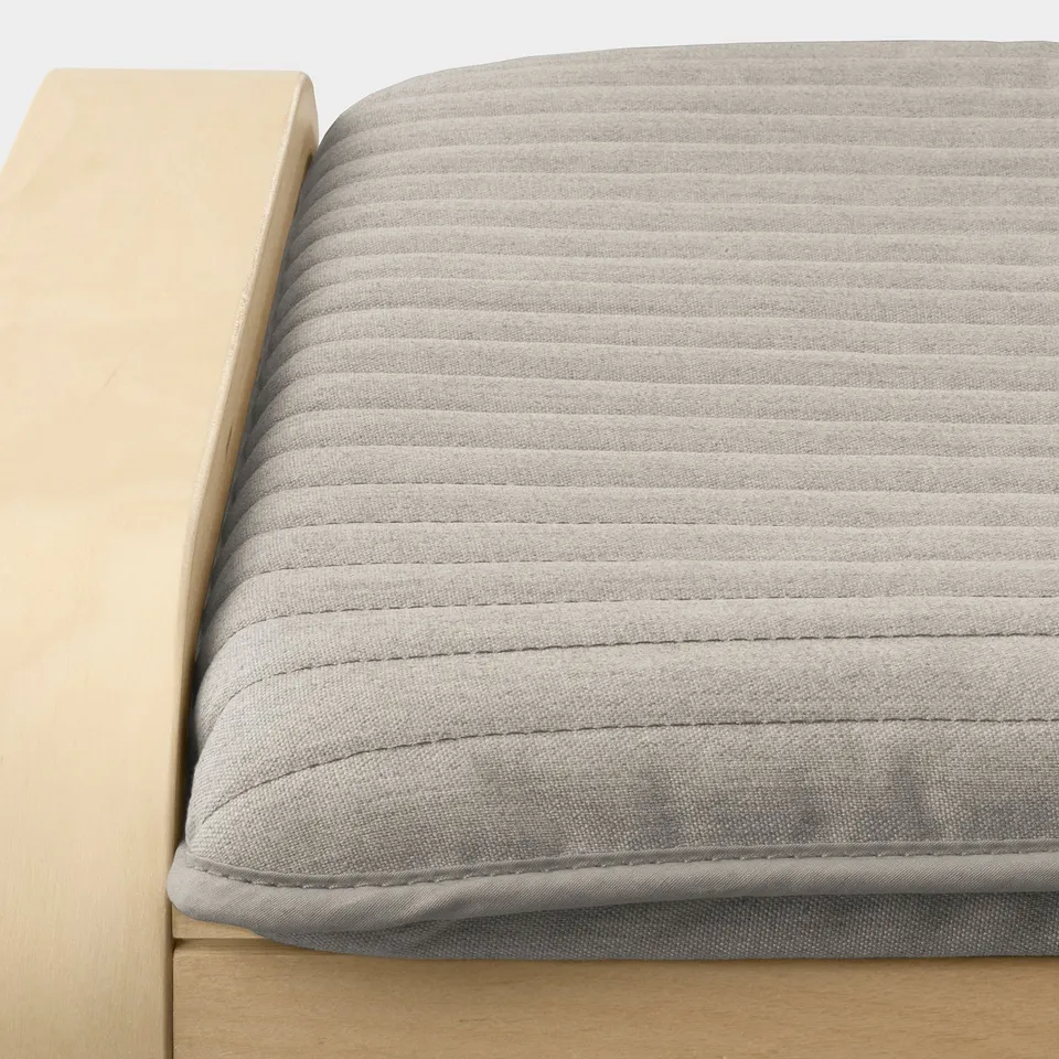 Close-up of cushioned chair with detailed stitching, light grey fabric, and wooden frame, emphasising comfort and quality.