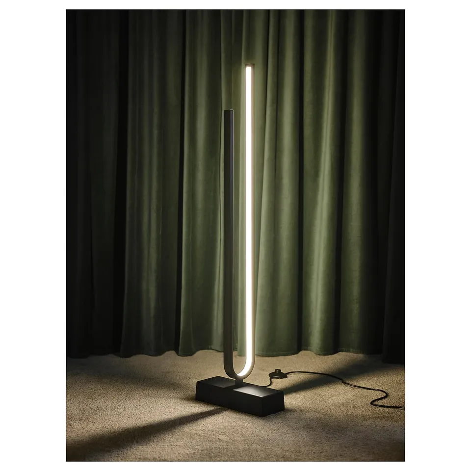 Modern floor lamp, slim white shape, led light, black base, green curtains, minimalist design.