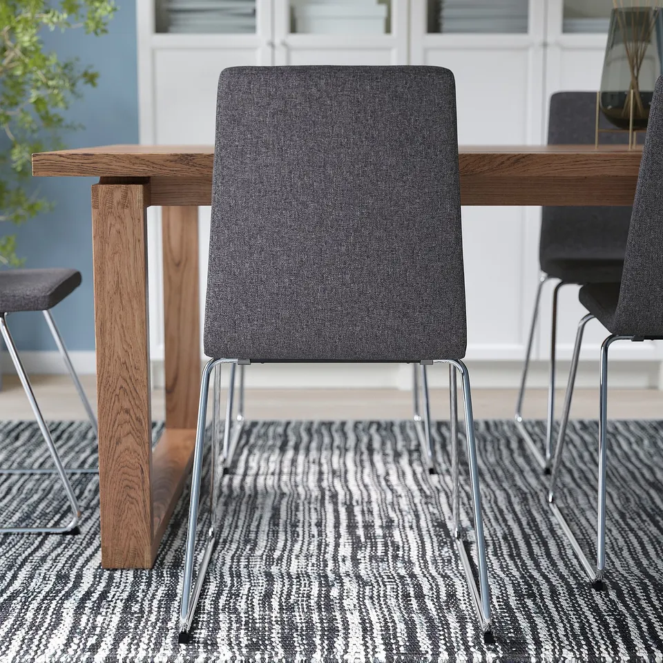 Modern dining setup with grey, padded LILLÅNÄS chairs around a wooden table on a patterned rug. Easy to clean and comfortable for daily use.