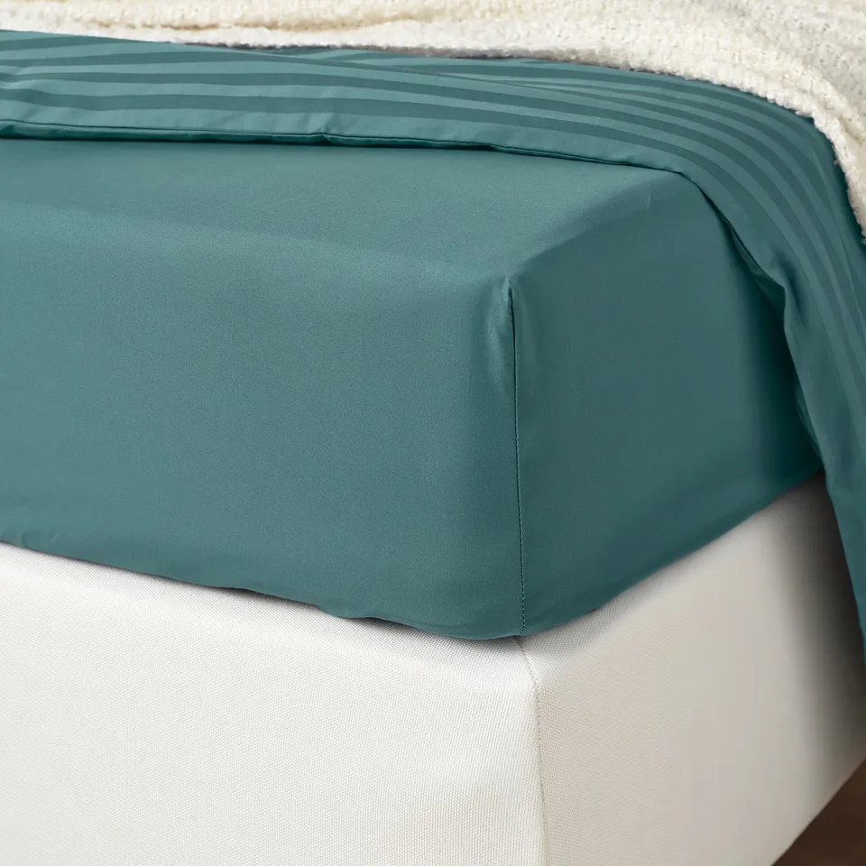 A teal fitted sheet with smooth fabric on a bed, showcasing its elastic edging.