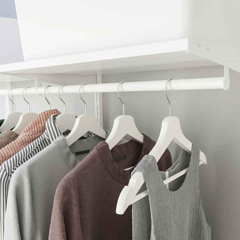 A closet with white hangers holding colourful shirts below a shelf.