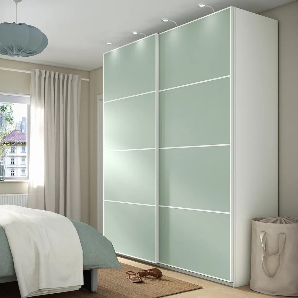 Modern bedroom with tall MEHAMN light green wardrobes featuring sliding glass doors. Wardrobes reach ceiling height, taller than bed and curtains.