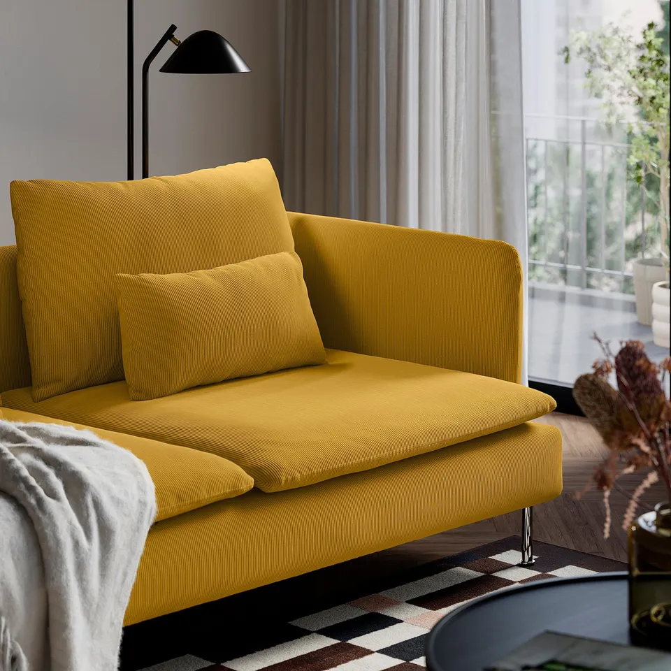 Mustard-yellow sofa with loose cushions stands on high legs, beside a tall black lamp.