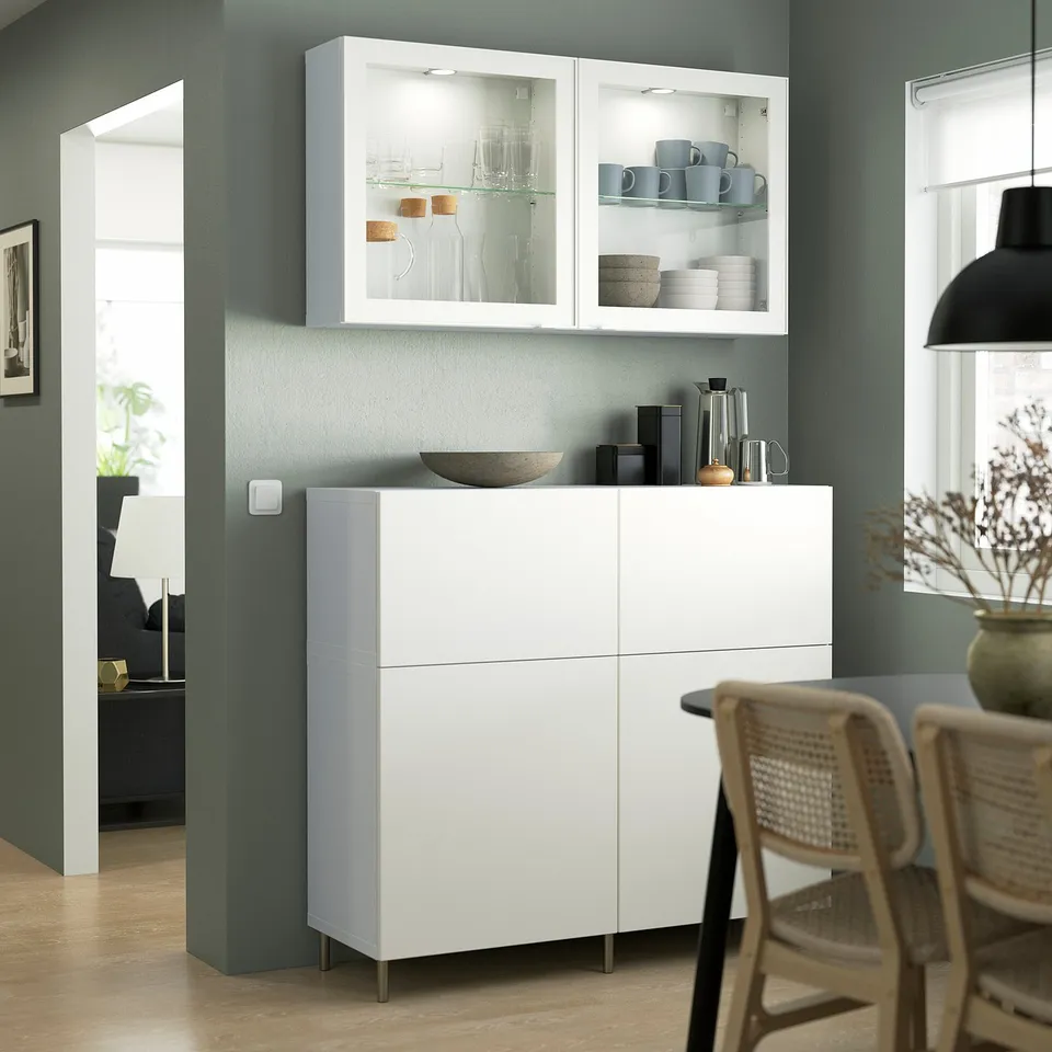 Modern living room with white ÖSARP cabinet & glass-door display, plates, mugs, bowl, and woven chairs.