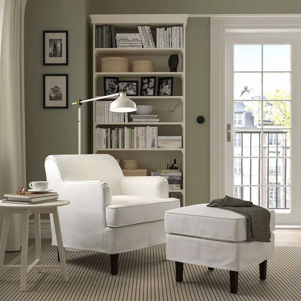 Cosy reading spot: white ROCKSJÖN armchair and footstool beside a bookshelf with natural light.