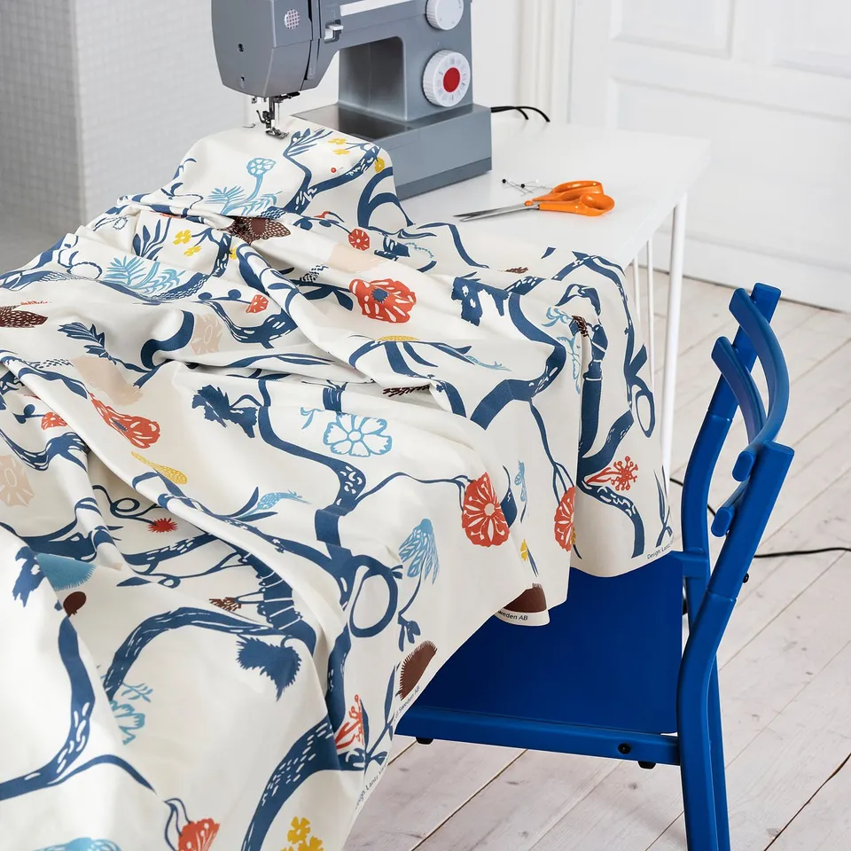 Colourful floral fabric spread on blue ironing board near sewing machine, ready for sewing project.