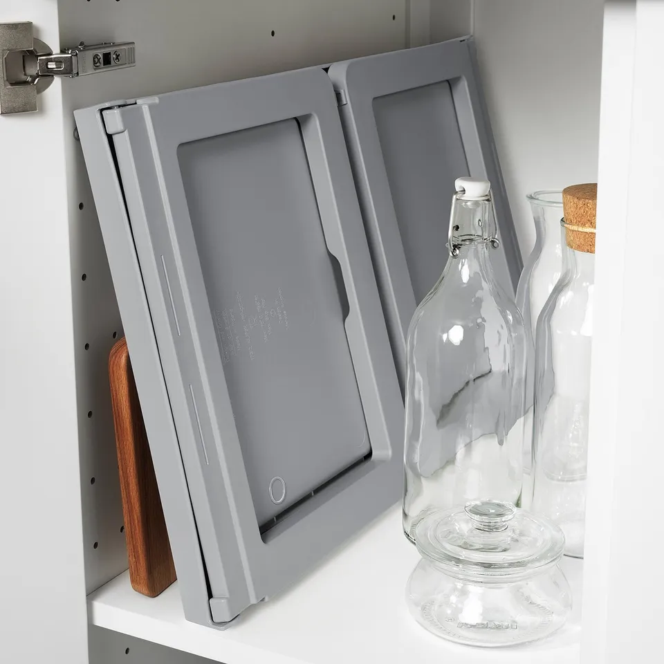 A grey KLIPSK bed tray stored upright on a shelf. It has foldable legs and a groove for holding a tablet or book.