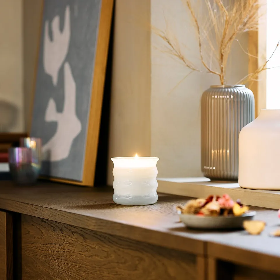 White scented candle, fruits, picture, vases with branches.
