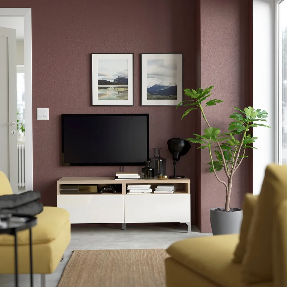 Modern living room with BESTÅ tv unit, yellow sofa, potted plant, and mountain art. Tv bench in white, tv black, wall dark red.
