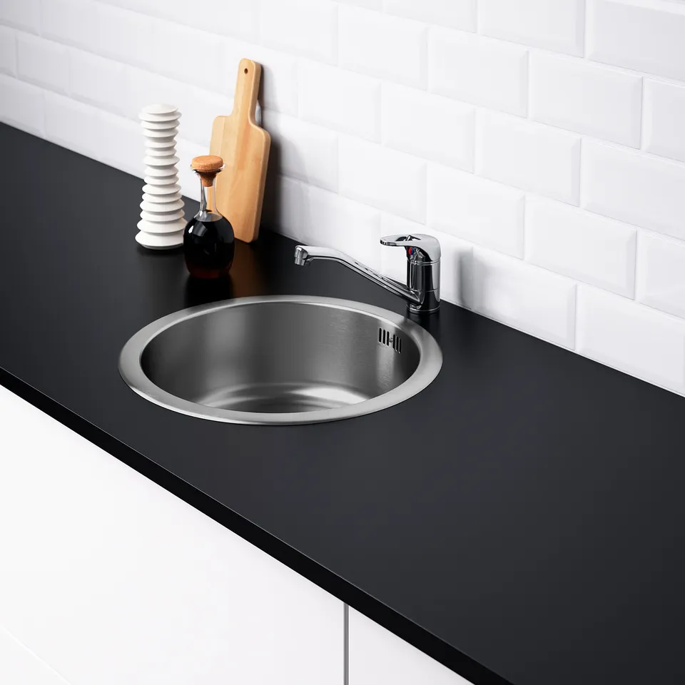 Stainless steel kitchen sink in black countertop with brushed nickel tap, highlighting its sleek design and included accessories.