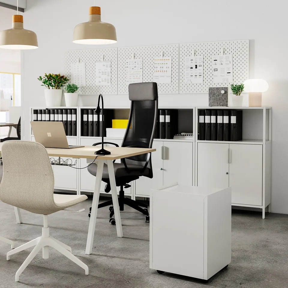 Modern office space with white TROTTEN metal storage units, beige chairs, and hanging lights.