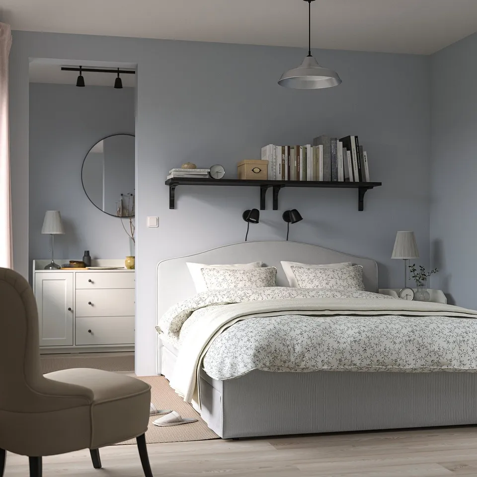 Modern grey bed, white linens, wooden chair, blue walls, bookshelf & dresser with mirror.