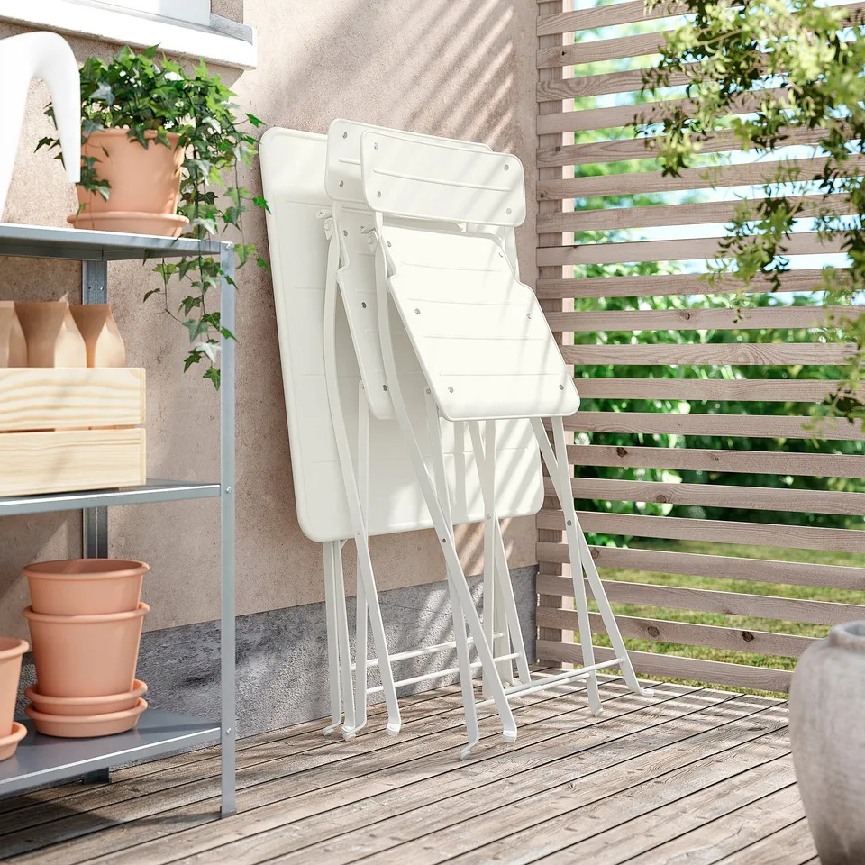 Two stacked white SUNDSÖ chairs on a wooden deck near a beige wall with shelves holding potted plants and decorative vases.