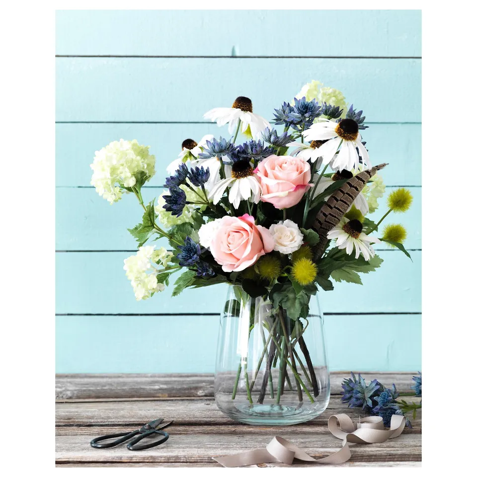 Beraekna vase with pink roses, white daisies, green leaves on wooden table.