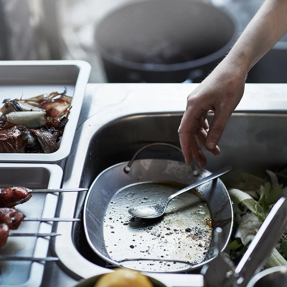 A person cooks in a stainless-steel kitchen with various tools and ingredients visible.