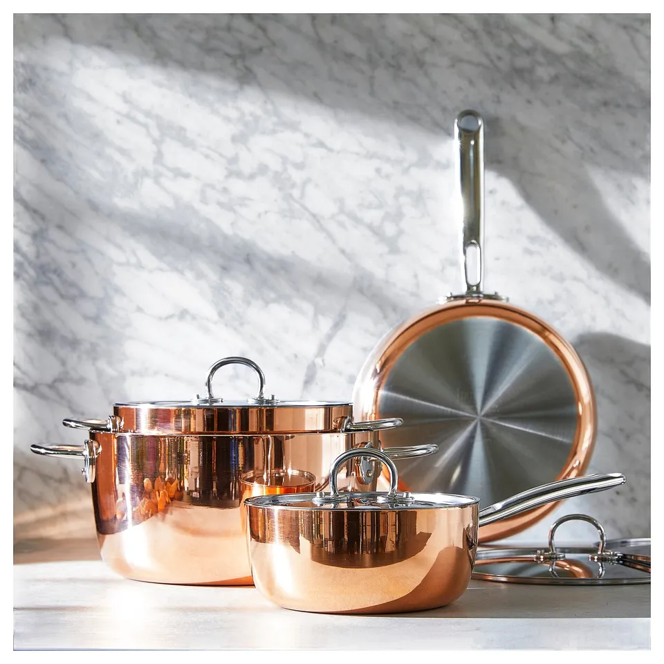 FINMAT copper kitchenware: shiny, stackable pots and pans with stainless steel handles and lids on a marble surface. Elegant, reflective design.