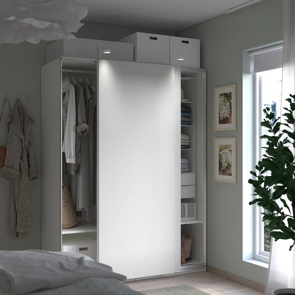 Modern bedroom with white PAX wardrobe, sliding doors, hanging clothes, shelves, plant, and grey walls.