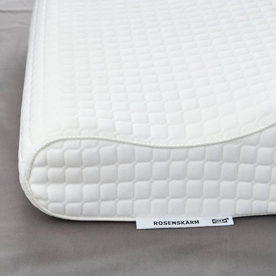 Close-up of the white rosenskarm pillow on a grey surface. Text labels product.