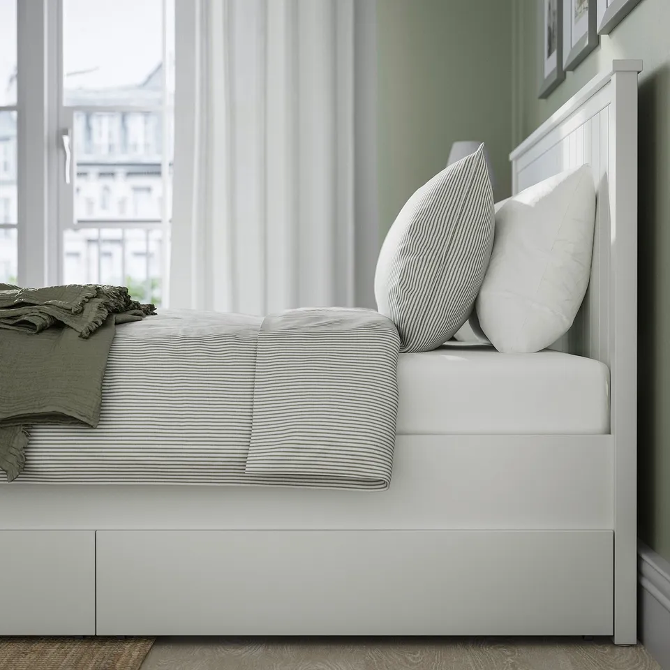 Bed with large storage drawers and headboard, neatly made with striped linens and decorated pillows.