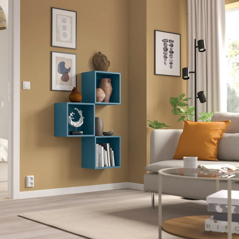 Stylish living room with blue EKET shelf, vases, books, grey sofa, orange pillow, coffee table, and art.