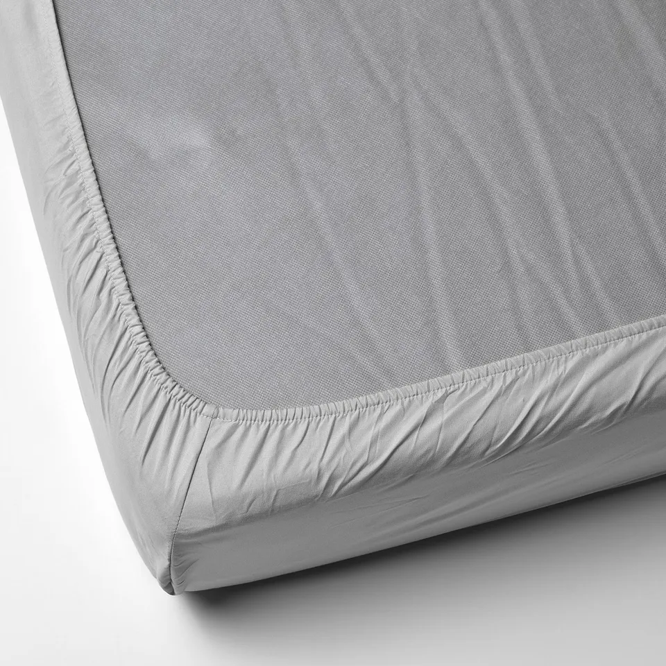 Grey fitted bed sheet with elastic edges, exhibited on a corner, made from recycled polyester.