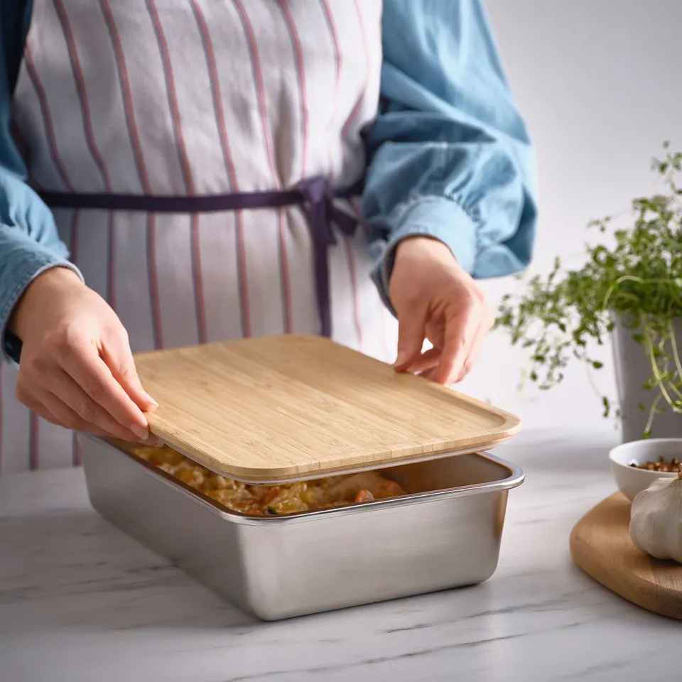 Person placing bamboo lid on rectangular food container, demonstrating its use for food storage.