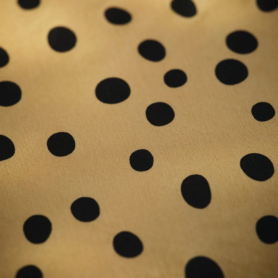 Close-up of a fitted sheet with large black spots on a beige background, showcasing its smooth texture and quality design.