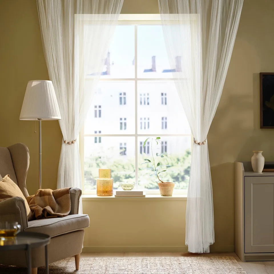 Cosy living room with large window, beige curtains, armchair, and warm light.