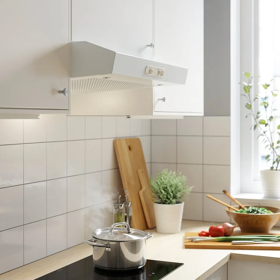 Modern white kitchen hood with led light mounts in cabinet, modern appliances on countertop.