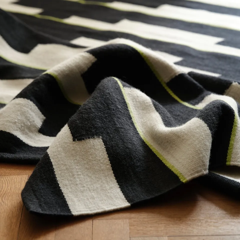 Handwoven wool rug displayed on wooden floor, showcasing high-quality craftsmanship with geometric patterns in black, white, and green.