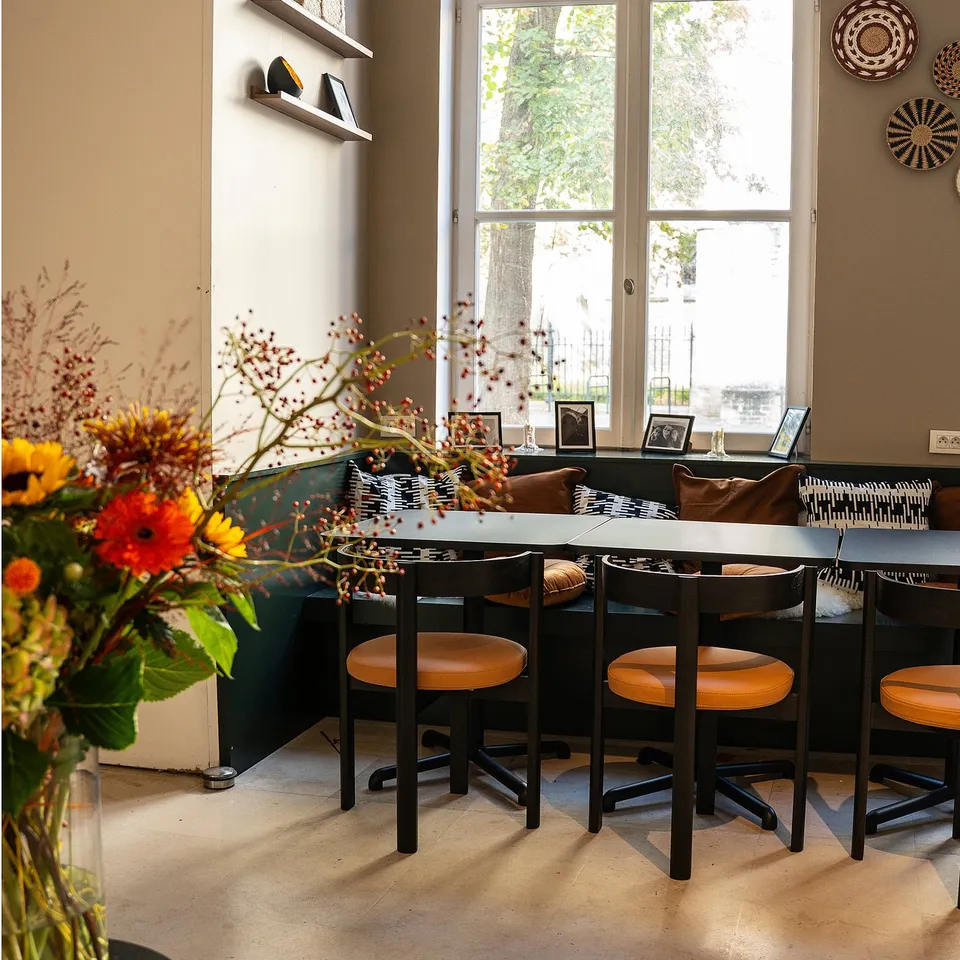 Modern café with moon-shaped black leather chairs & minimalist design. Colourful flowers & large windows enhance warm vibes.