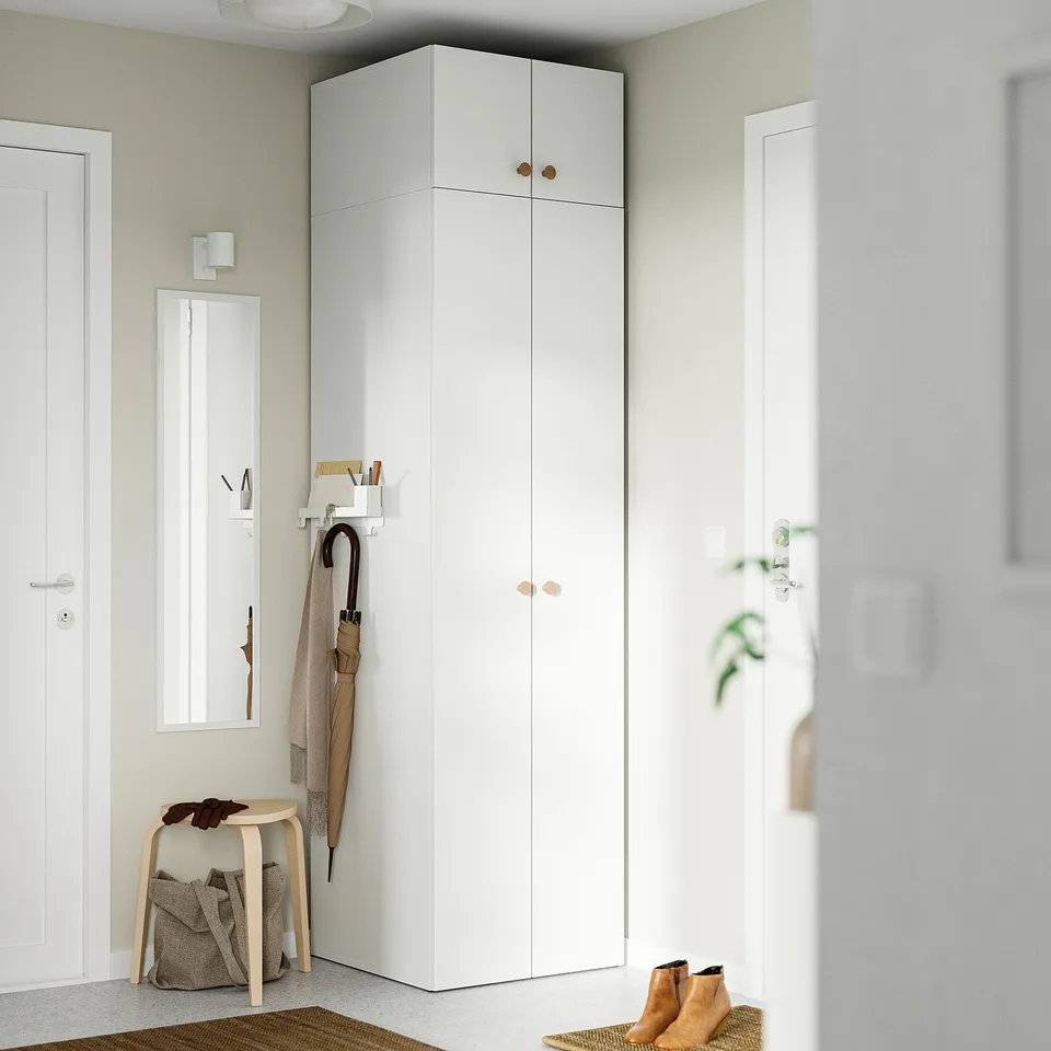 Tall white LASTARE wardrobe in hallway, surrounded by smaller doors. Holds clothes, with brown boots and umbrella nearby.