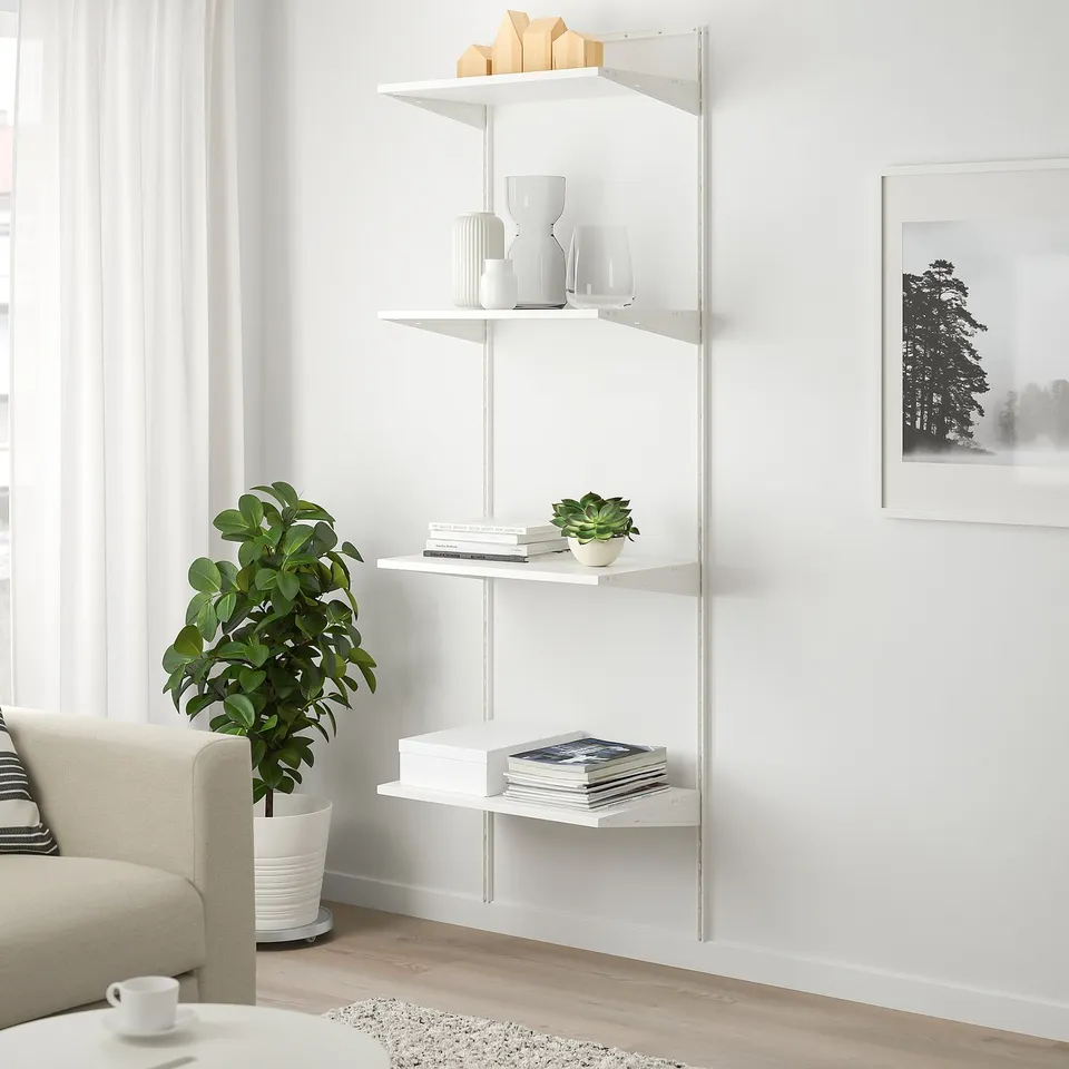 White BOAXEL shelving unit with 4 tiers and various items near beige sofa and window.