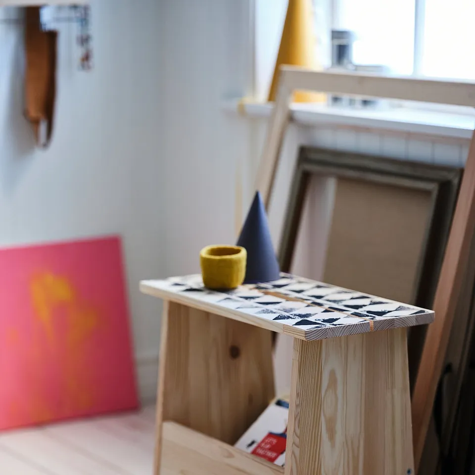 Wooden PERJOHAN stool, multicoloured top, yellow cup, blue cone, red art, by fireplace.