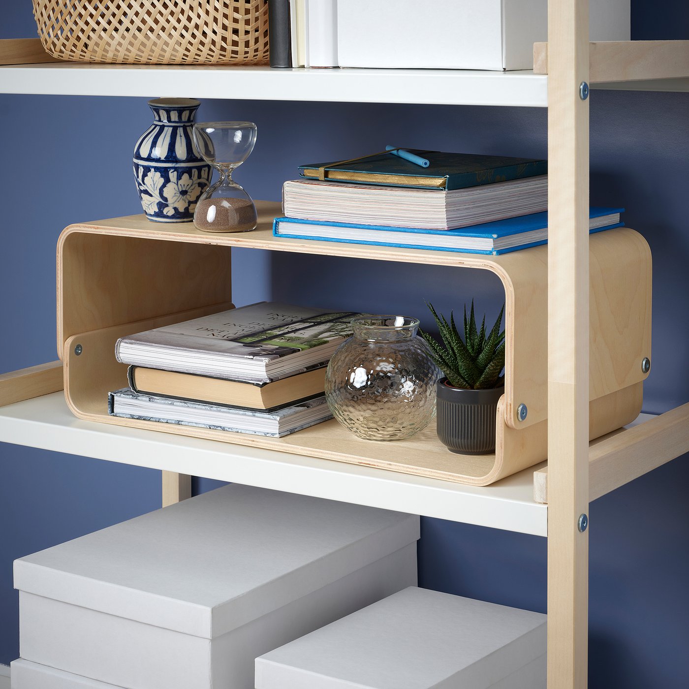 Wooden bookshelf with curved divider holding books, decorative vases, and small plant.