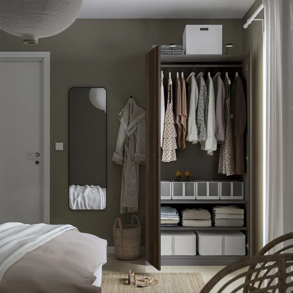 Bedroom with open wardrobe displaying clothes, folded fabrics, and storage boxes. Mirror and hanging robe nearby.
