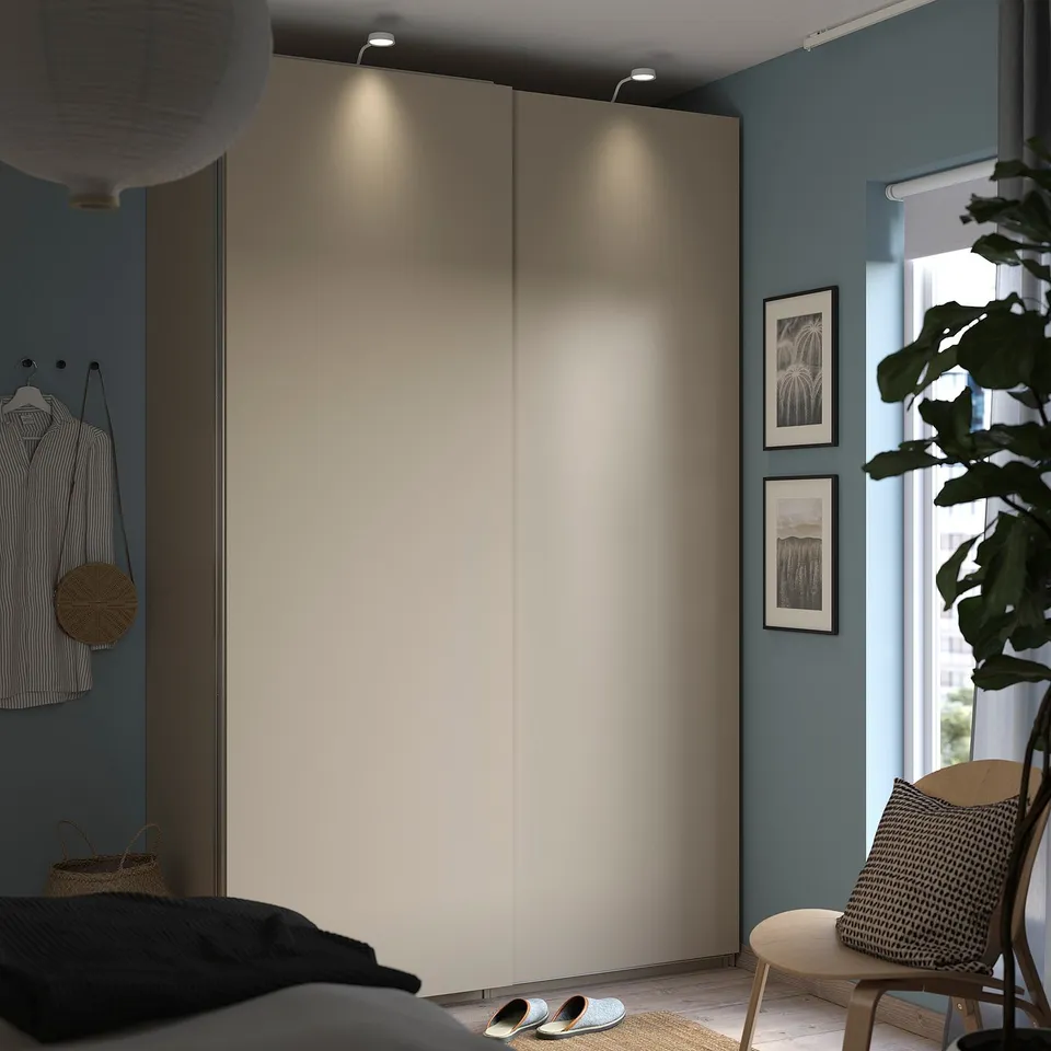 Modern bedroom with light grey PAX wardrobe, plants, black bedding, striped shirt, and wooden chair.