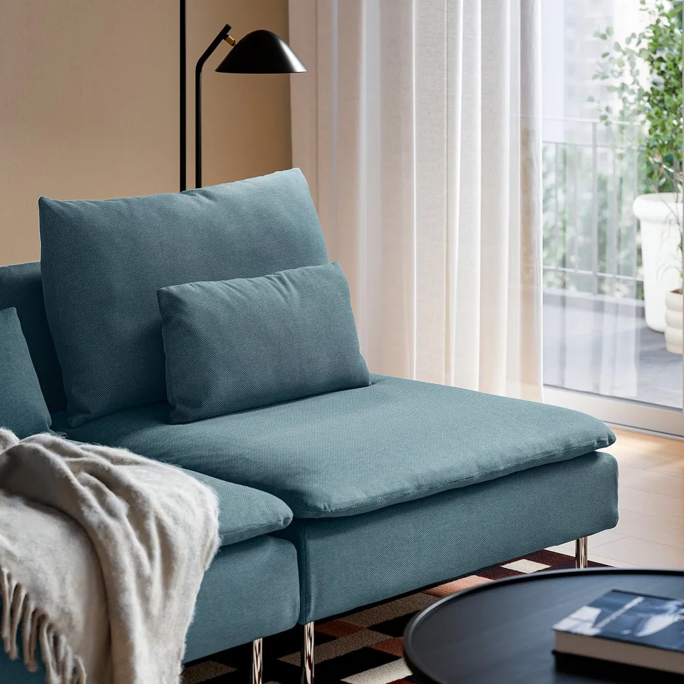 Blue sofa with two cushions, blanket, and floor lamp; windows with curtains.