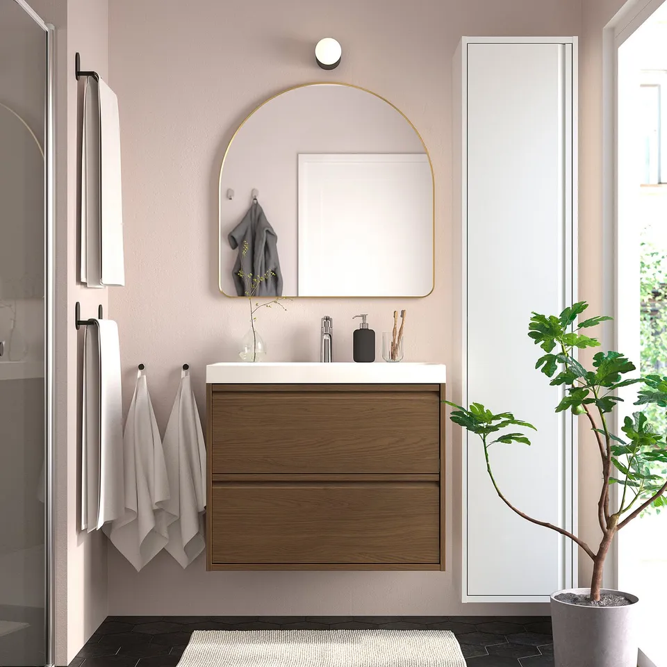 Modern bathroom with LINDBYN arch mirror, white, wall-mounted, wood cabinet, grey plant, and hanging towels.