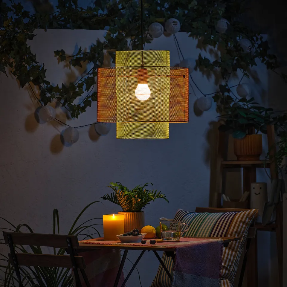 Small outdoor table set with striped chairs, hanging light, plants, and candle, creating a cosy evening ambiance.