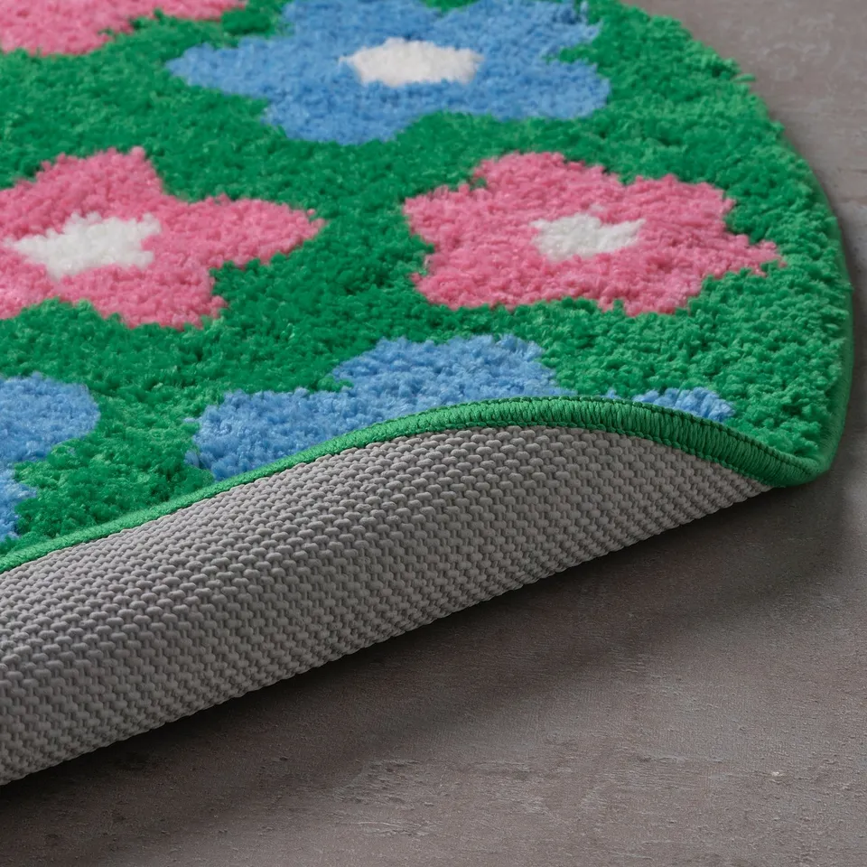 Colourful flower-patterned bath mat with thick, soft pile for warmth and comfort. Pink flowers, green leaves, and blue sky with clouds.