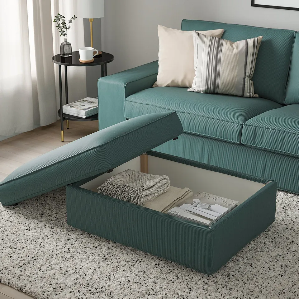 Cosy living room with teal sofa, footstool with hidden storage, striped pillows, and side table with lamp.